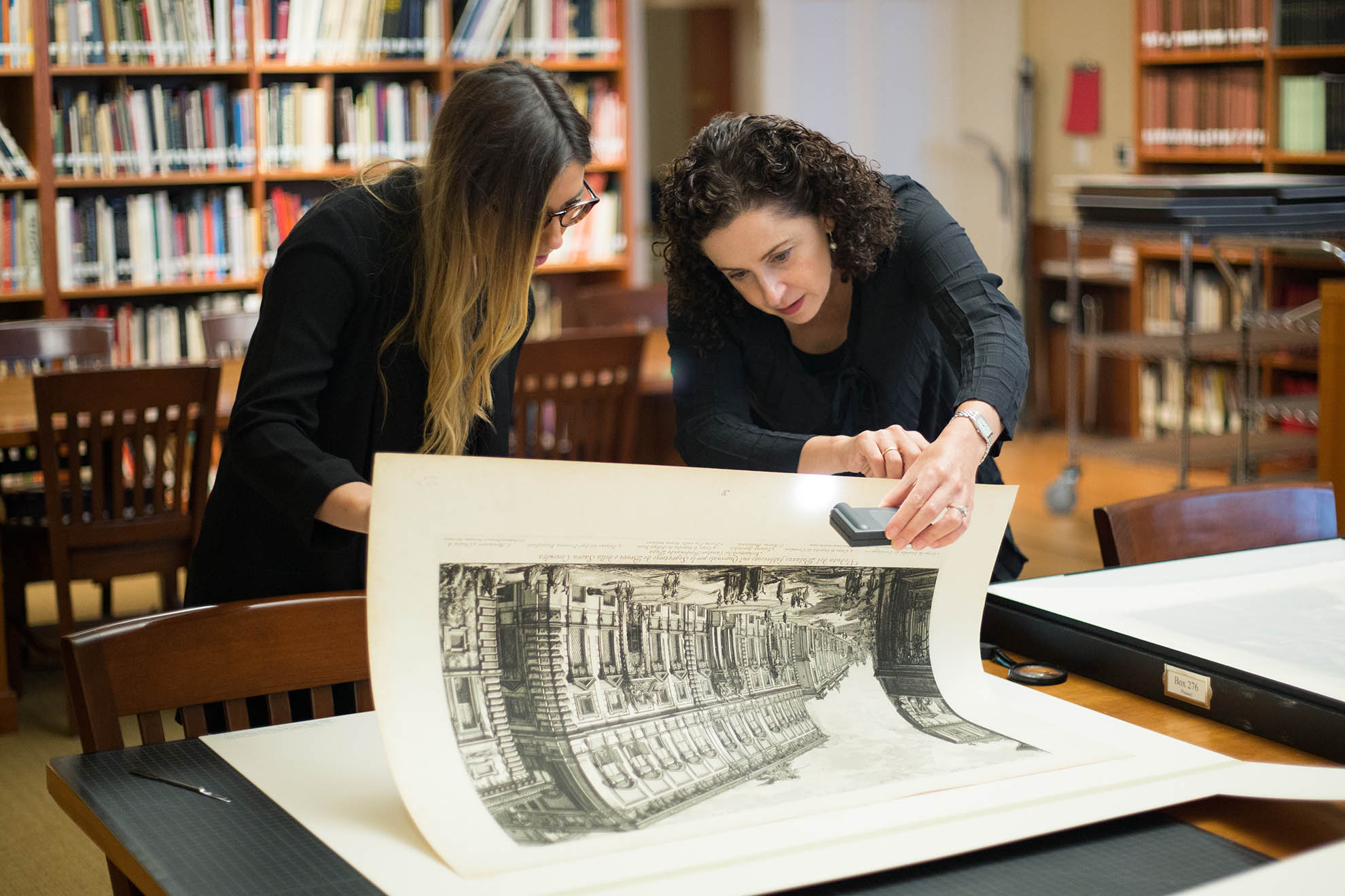 Photo of two people looking closely at a large print